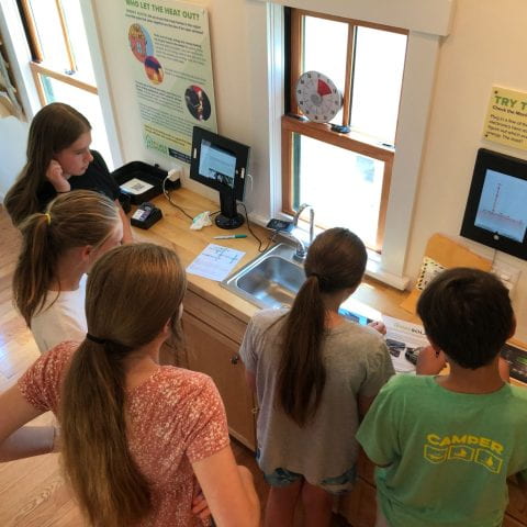 Five students inside the PowerHouse look at educational materials and screens charting energy usage and solar energy. 