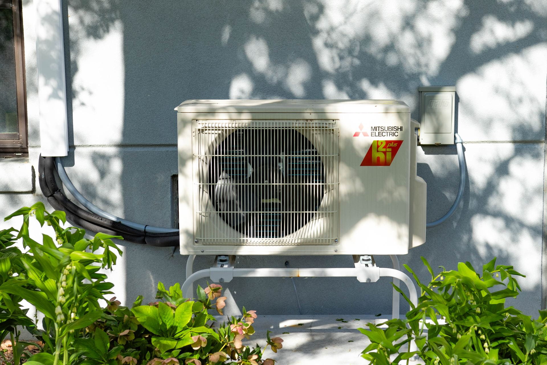 An image of a heat pump with foliage nearby