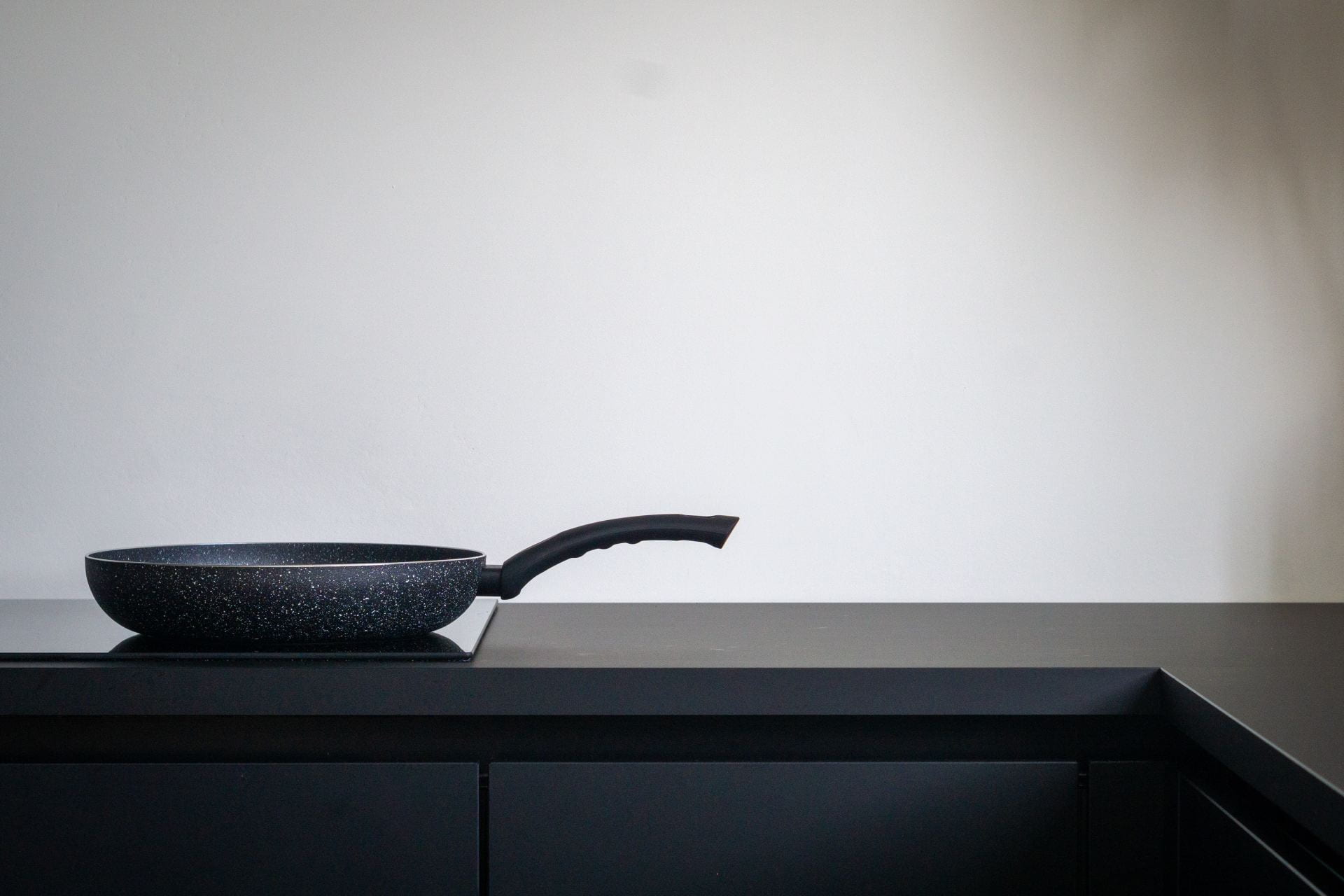 An image of a sleek, black induction cooktop with a black skillet on it